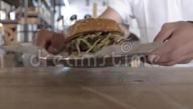 特写男人把一个盘子和一个汉堡放在桌子上，准备吃一个汉堡。 盘子里有多汁的汉堡。 4k. 4k录像。 60英尺